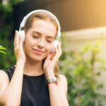 Smiling woman listening to music with headphones in sunny garden setting.