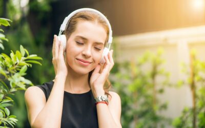 Cómo afecta la música al cerebro Smiling woman listening to music with headphones in sunny garden setting.