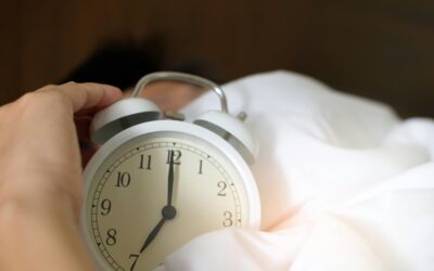 A close-up of a hand reaching for a ringing alarm clock, symbolizing waking up in the morning.