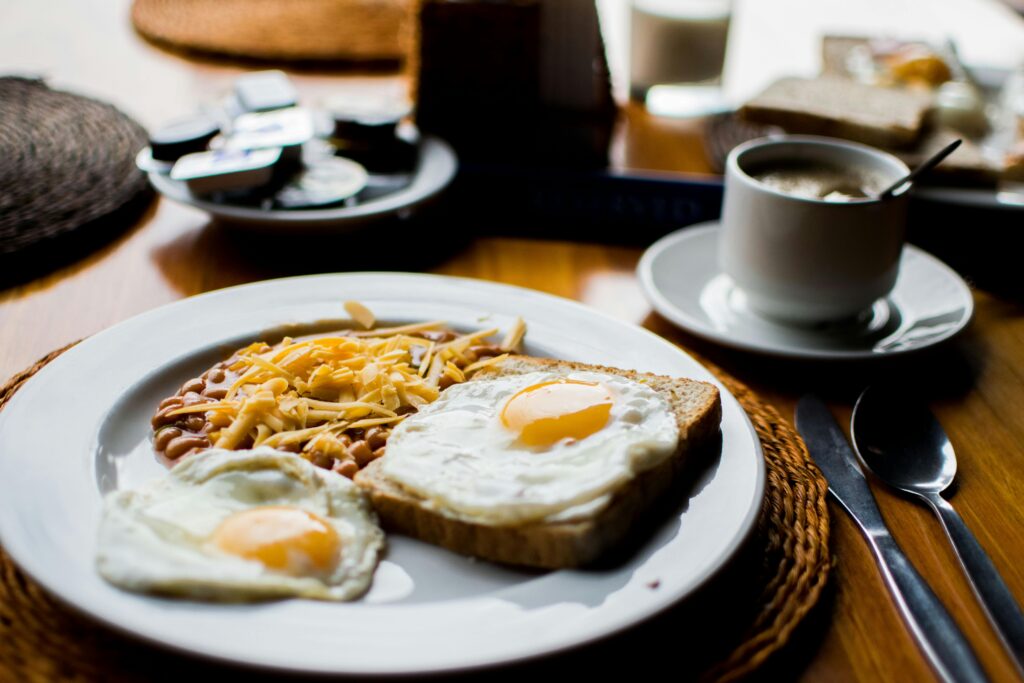 Un abundante desayuno con huevos fritos, frijoles horneados y tostadas servidas con café en un ambiente acogedor.