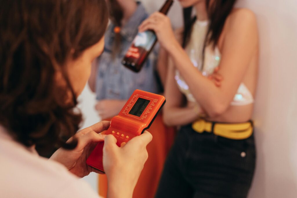 Una donna a una festa che tiene e gioca a un dispositivo di gioco portatile vintage, creando un'atmosfera nostalgica.