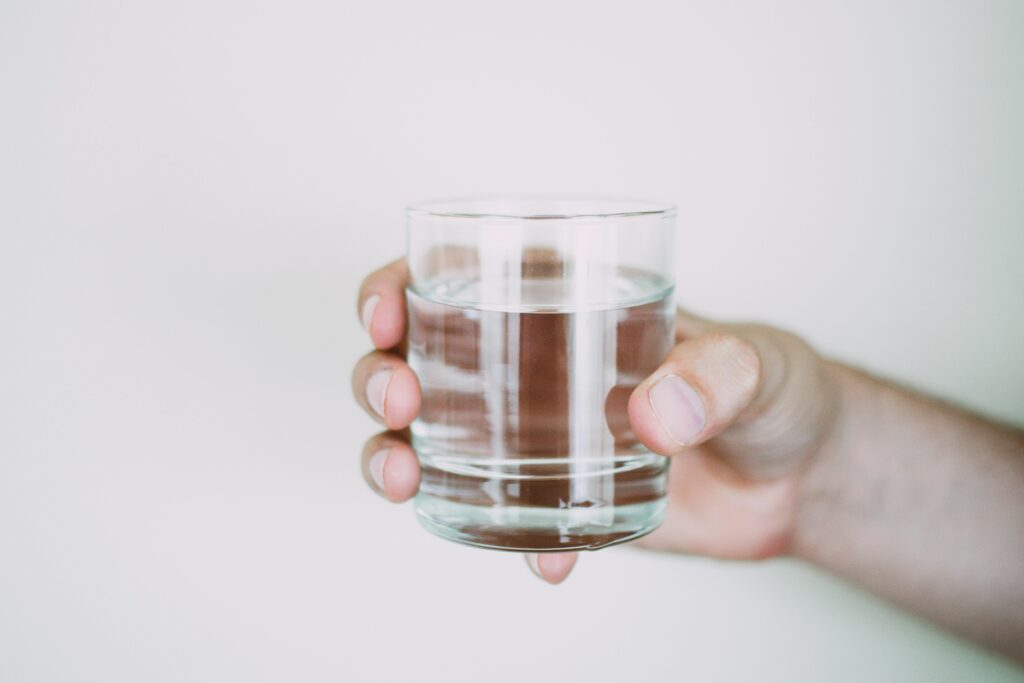 Un primer plano de una mano sosteniendo un vaso de agua transparente, que simboliza el refresco.