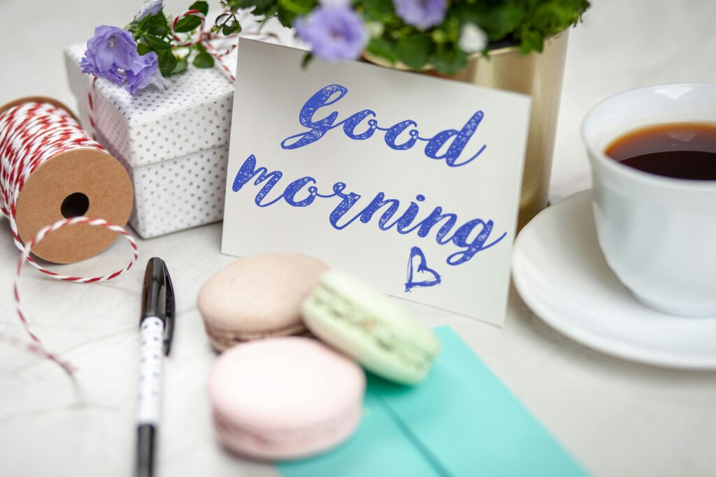 Tarjeta de buenos días con café, macarons y regalos creando una escena acogedora.