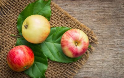 Three ripe apples on leaves over a rustic wooden background, emphasizing freshness and nutrition.