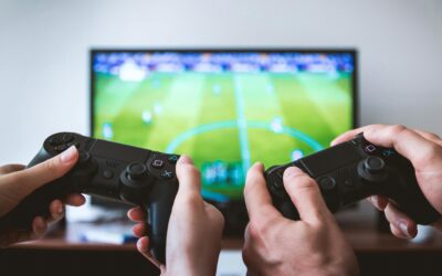 Close-up of hands holding gaming controllers in front of a TV. Engaged in a video gaming session.