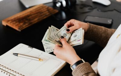 Guía para principiantes sobre ingresos pasivos Unrecognizable elegant female in sweater counting dollar bills while sitting at wooden table with planner and pen