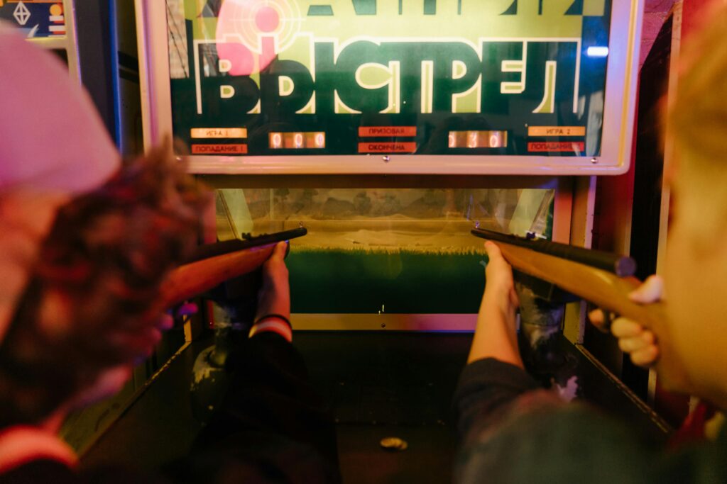 Adolescenti che si divertono a giocare a un gioco di tiro arcade vintage con fucili in un parco giochi arcade.