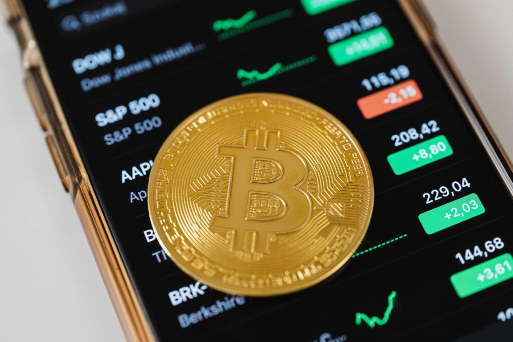 Un primer plano de una moneda de Bitcoin colocada en un dispositivo móvil que muestra datos de negociación del mercado de valores.