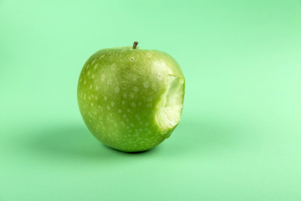Una manzana verde fresca y mordida sobre una simple superficie verde. Perfecto para la salud y el diseño temático de alimentos.