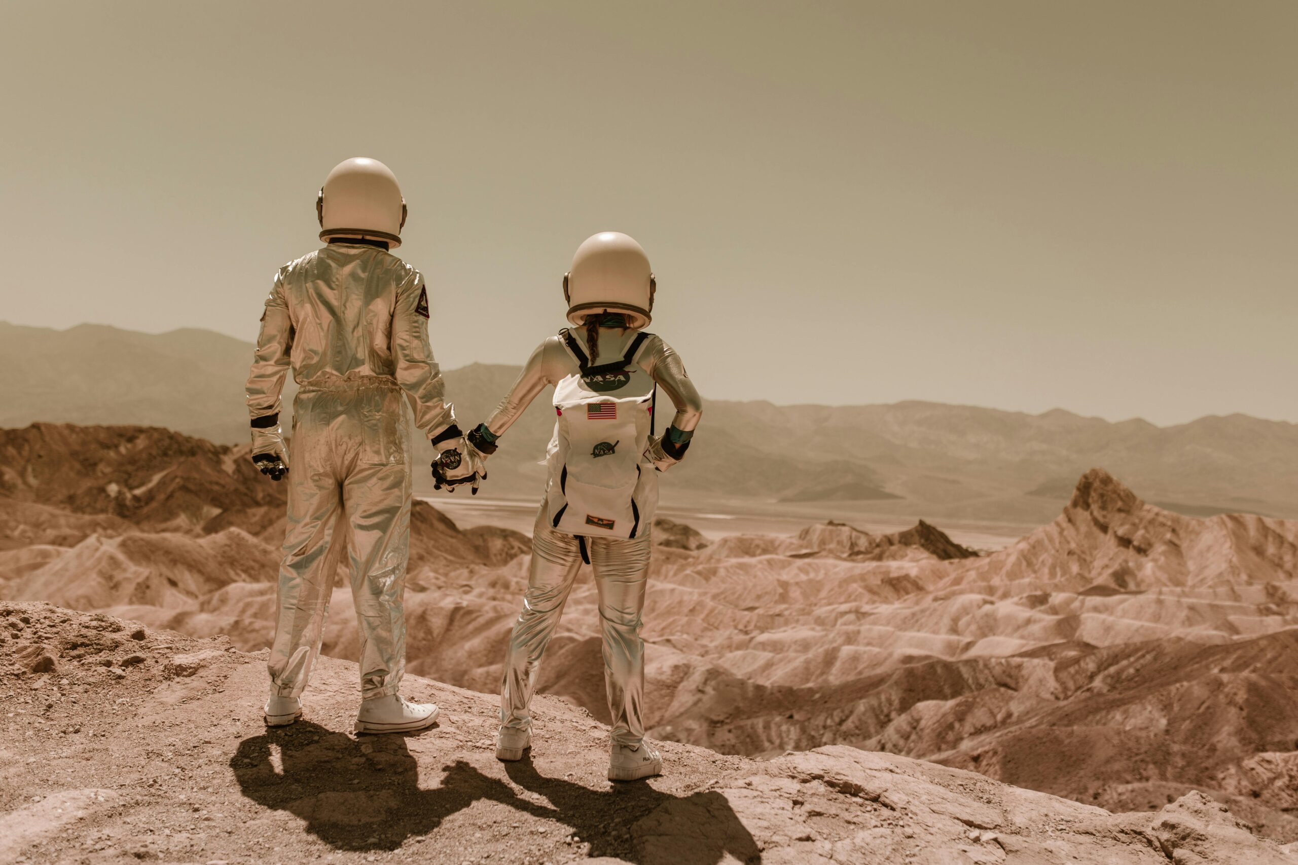 Two astronauts holding hands while exploring a desert terrain under a clear sky.